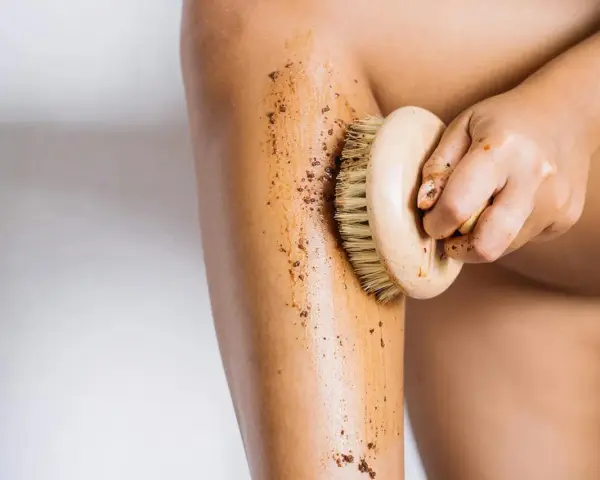 Exfoliación corporal con un cepillo de madera y un scrub para ayudar a como hidratar la piel desde dentro.