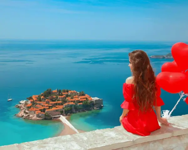 Marzenie o czarnogóra all inclusive samolotem? Kobieta w czerwonej sukni z sercami w ręku podziwia wyspę Sveti Stefan.