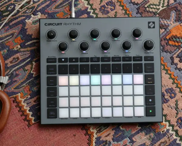 Szary kontroler Circuit Rhythm z podświetlanymi padami, gotowy do tworzenia muzyki. Słuchawki obok dopełniają scenę.