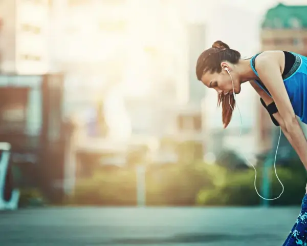 Atleta esausta appoggiata a un corrimano, con le cuffie. Potrebbe aver bisogno di rimedi per il sovrallenamento.