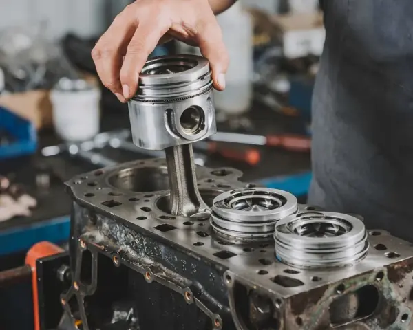 Mechanik montuje tłok do bloku silnika. Na bloku leżą inne tłoki.