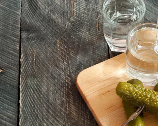 Zwei Gläser Wodka und eingelegte Gurken auf einem Holzbrett. Perfekt für alle, die Wodka selber machen wollen.