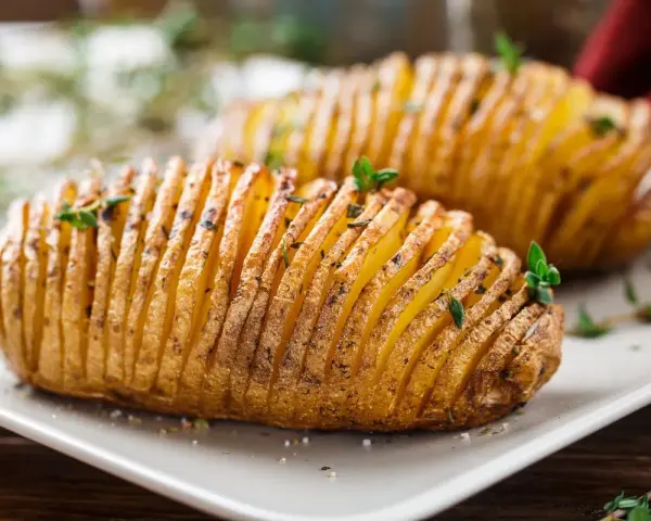 Patate hasselback dorate e croccanti, appena sfornate dalla friggitrice ad aria, guarnite con erbe aromatiche fresche.