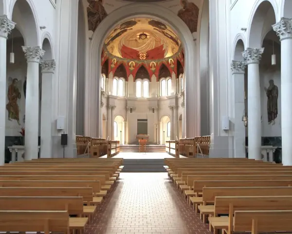 Interior of a grand abbey, with rows of wooden pews leading to an altar. The domed ceiling features a vibrant fresco. Check the abbey mass schedule for service times.