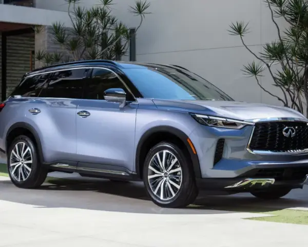 Elegancki, srebrny Infiniti SUV zaparkowany przed nowoczesnym domem z bujną roślinnością.