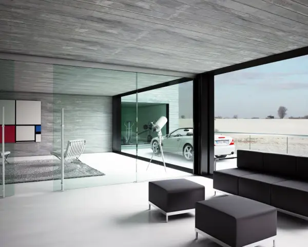 Interior moderno con sofá negro, sillones y una gran pared de cristal que da a un paisaje nevado y un coche descapotable.