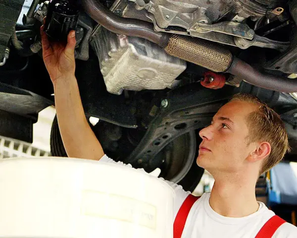Ein junger Mechaniker bei einer Arbeitsstunde in der Kfz Werkstatt wechselt den Ölfilter unter einem Auto.