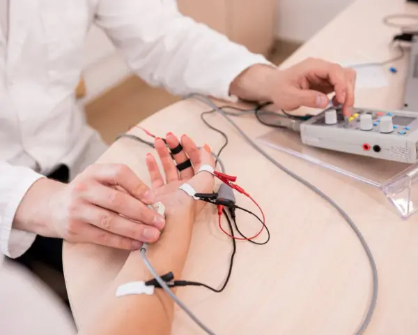 Lekarz wykonuje próbę tężyczkową, podłączając elektrody do dłoni pacjenta i regulując aparat.