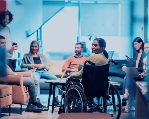 Ein Team bespricht sich, eine Frau im Rollstuhl ist integriert. Ein leidensgerechter Arbeitsplatz, an dem alle willkommen sind.