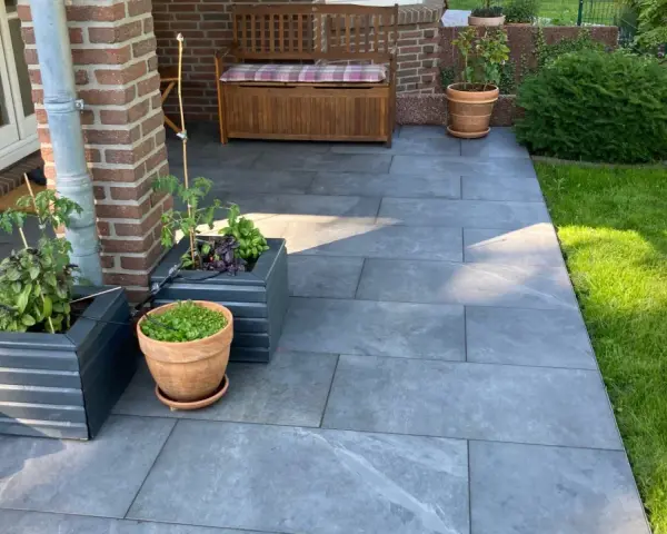 Moderne Terrassenplatten grenzen an einen gepflegten Rasen. Pflanzen in Töpfen und ein Holzbänkchen bieten schöne Rasenkante Ideen.