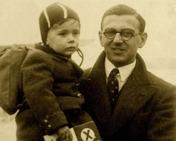Nick Winton porte un enfant sur son bras, un petit garçon avec un sac à dos, prêt pour un nouveau départ.