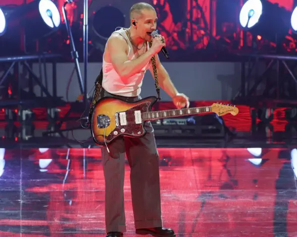 Krzysztof Zalewski na koncercie, śpiewa i gra na gitarze. Scena oświetlona czerwonymi światłami.