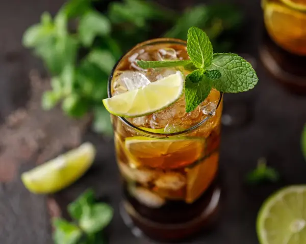 Szklanka z drinkiem Cuba Libre, lodem, plasterkami limonki i miętą.