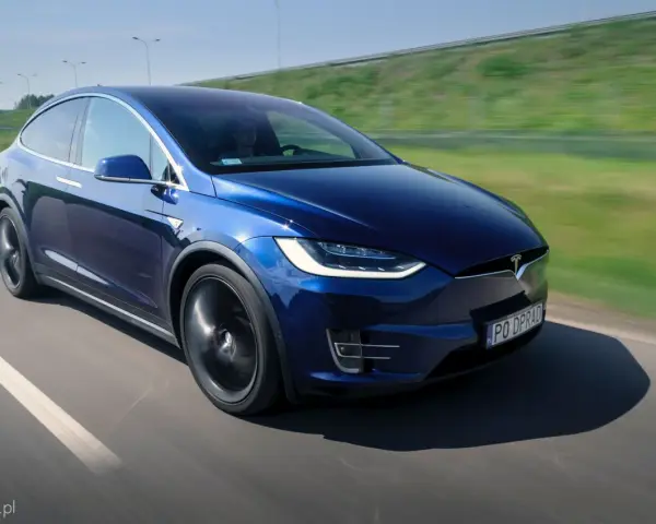 Granatowy Tesla Model X w ruchu na drodze, z widocznym kierowcą.