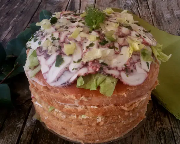 Panettone Gastronomico with sliced octopus, lettuce, and herbs on a wooden table.