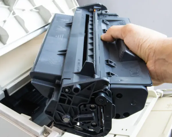 Ręka wyjmuje czarny toner z drukarki. Skorzystaj z naszej oferty bezpłatny odbiór tonerów.