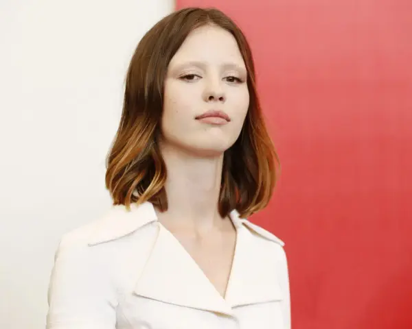 La giovane attrice protagonista del film di mia goth, con capelli castani mossi e un'espressione intensa, indossa un abito bianco.