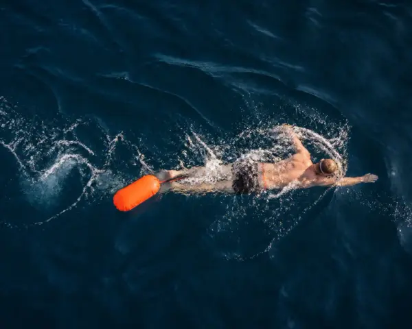 Un nageur profite d'une séance de nage en eau libre, suivi d'une bouée orange vif.