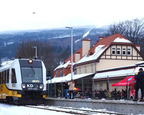 Pociąg GRYFC na stacji w Świeradowie-Zdroju, zimowy krajobraz z ośnieżonymi górami w tle.