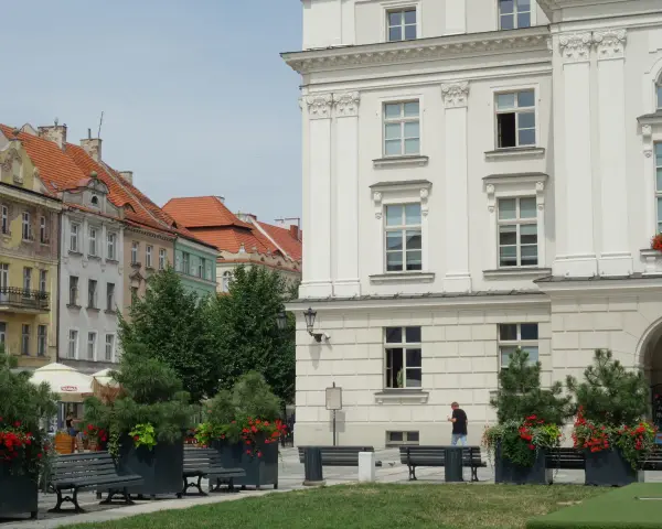 Urokliwe miasto nad Prosną z zabytkową architekturą, zielenią i ławkami w centrum.