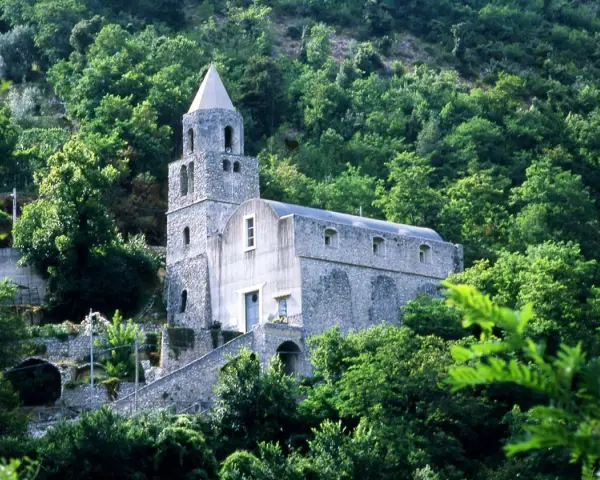 Antica chiesa in pietra su un fianco di montagna, circondata da alberi lussureggianti. I tramonti montagna qui sono magici.