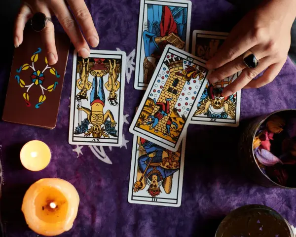 Manos de tarotista que es, barajando cartas y velas encendidas sobre tela morada.
