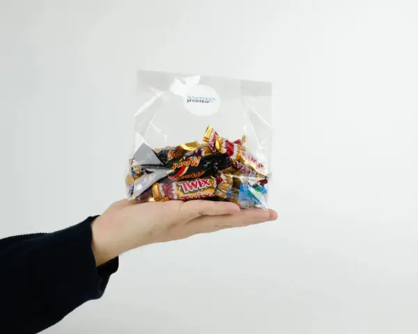 En hand håller en presentkorg i cellofan fylld med choklad.