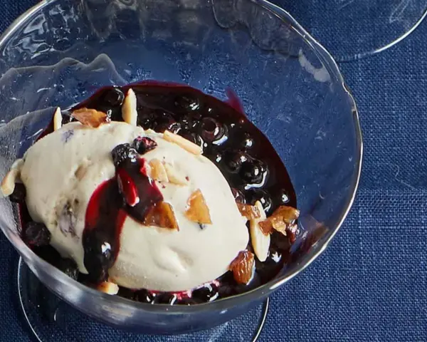 Cremiges Malaga Eis Rezept mit Blaubeersauce und Mandelsplittern in einer Glasschale.