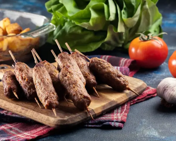 Aksamitne ćevapi na drewnianej desce, obok pomidory, czosnek i pieczone ziemniaki. Pyszny posiłek gotowy do podania.