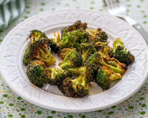 Brocoli en airfryer, crujiente y dorado, servido en un plato blanco con un mantel verde.