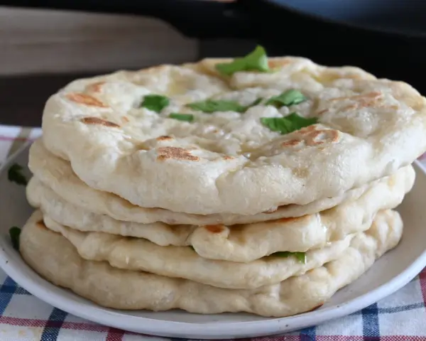 Pila di pane in padella, soffice e dorato, guarnito con erbe fresche. Perfetto per accompagnare ogni pasto.