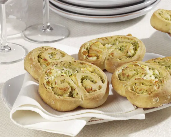 Zucchini Schnecken mit Käsefüllung auf einem Teller mit weißer Serviette.