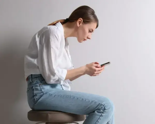 Frau mit gebeugtem Rücken und Handy. Schlechte Haltung kann zu einem Buckel im Nacken Ursache sein.