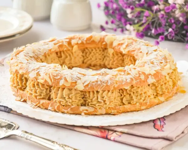Un delicioso praliné que es un pastel Paris-Brest, cubierto de almendras laminadas y espolvoreado con azúcar glas.