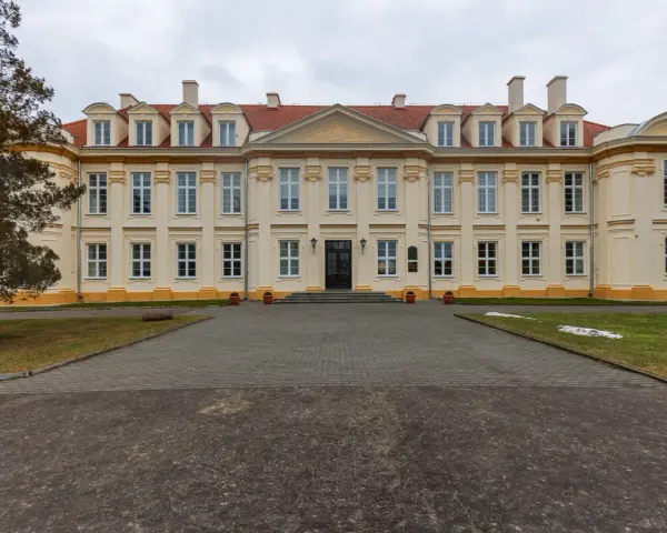 Pałac biskupów kujawskich w Wolborzu, okazała budowla z żółtą fasadą i czerwonym dachem, otoczona zielenią i brukowanym podjazdem.