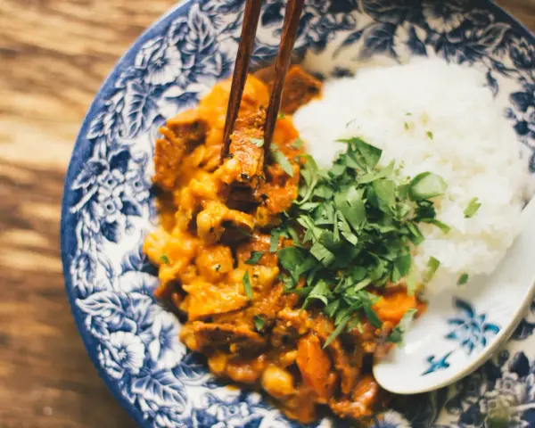 Miseczka z ryżem i curry, podana z posiekaną natką pietruszki, jedzona pałeczkami.