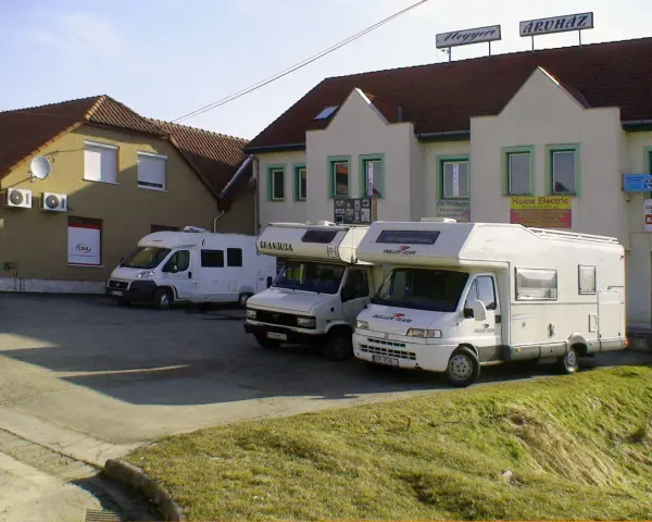 Trzy białe kampery zaparkowane przed budynkami z szyldami.