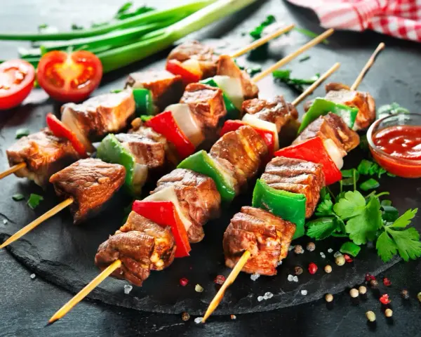 Spiedini di carne succulenti con peperoni e cipolle, pronti per essere gustati con una salsa rossa e pomodorini freschi.