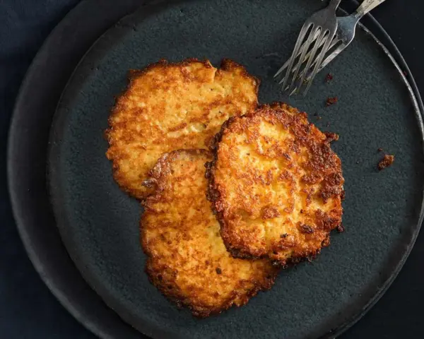 Drei goldbraune Kartoffelpuffer, frisch zubereitet im Thermomix, liegen auf einem dunklen Teller.