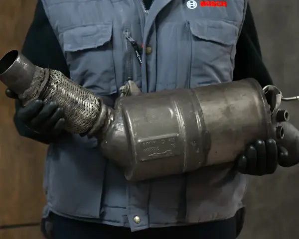 Mechanik w rękawiczkach trzyma zużyty element układu wydechowego, prawdopodobnie po problemach z wypalaniem DPF.