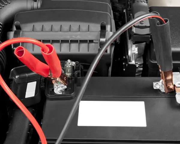 Jumper cables connected to a car battery. Learn how long to leave jumper cables on for a successful jump start.