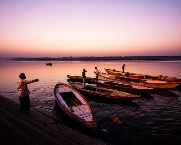 Vue d'ensemble de bateaux amarrés sur un fleuve au crépuscule, avec des silhouettes humaines sur la rive. Ces photos grand angle capturent la sérénité du moment.