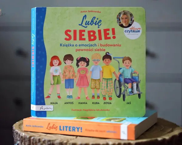 Książka "Lubię SIEBIE!" Anny Jankowskiej to pomoc w budowaniu pewności siebie u dzieci. Ilustracje przedstawiają grupę uśmiechniętych dzieci, w tym chłopca na wózku.