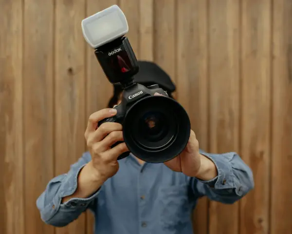Fotograf trzyma aparat Canon z lampą błyskową. Liczba przewodnia lampy błyskowej jest kluczowa dla uzyskania idealnego oświetlenia.