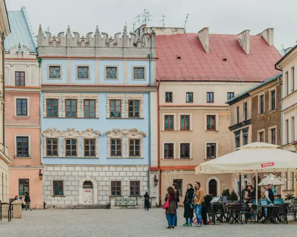 Kolorowe kamienice na rynku, idealne na tani city break. Ludzie spacerują, siedzą w ogródku kawiarnianym.