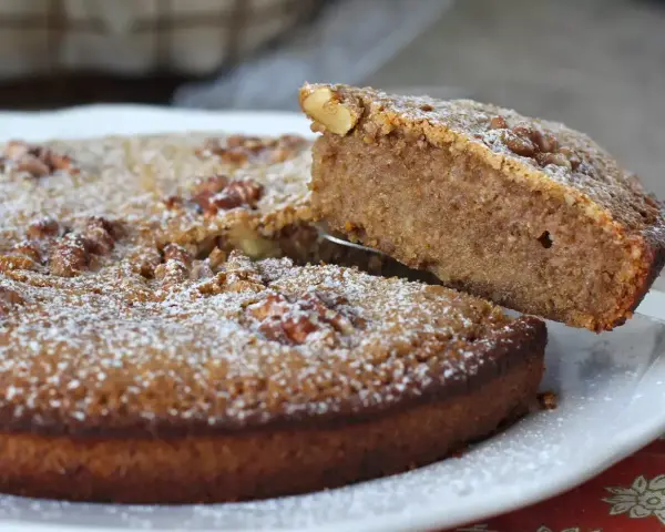 Une part est soulevée d'un délicieux gâteau aux noix, saupoudré de sucre glace.