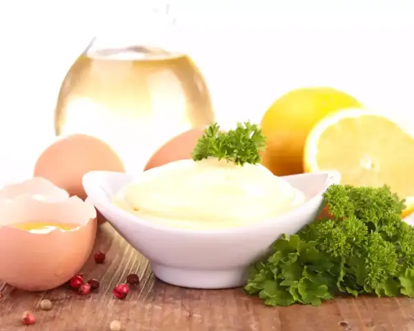 Un bol de mayonnaise maison crémeuse, entouré d'œufs, de citron, d'huile et de persil.