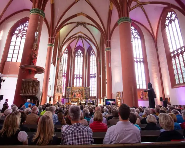 Menschen sitzen in einer Kirche, die für eine Veranstaltung beleuchtet ist. Es ist schön, dass man wieder in die Kirche eintreten kann.