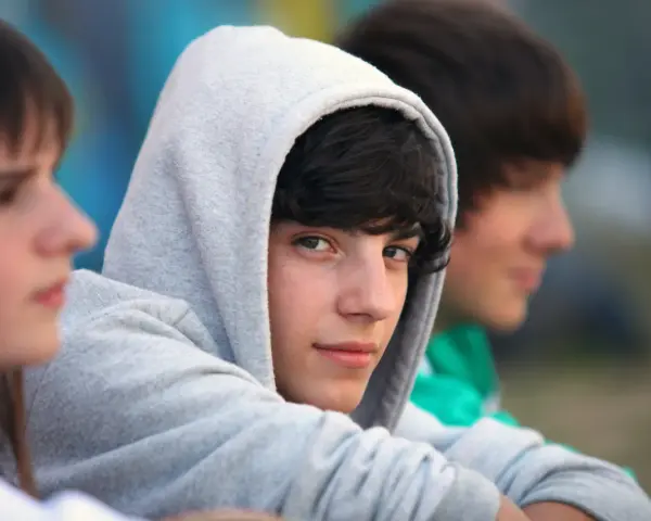 Drei Jungs, etwa 13 Jahre alt, sitzen nebeneinander. Einer trägt einen grauen Kapuzenpullover, der sein Gesicht fast verdeckt.