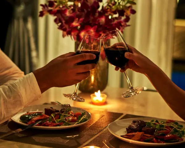 Para wznosząca toast kieliszkami z czerwonym winem podczas romantycznej kolacji przy świecach.